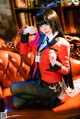 A woman in a red jacket and black skirt sitting on a couch.