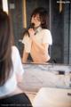 A woman in a white shirt is brushing her teeth in front of a mirror.