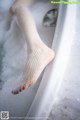 A woman in fishnet stockings is sitting in a bathtub.