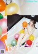 A naked woman sitting in a bathtub surrounded by balloons.