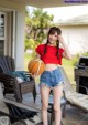 A woman in a red shirt and denim shorts holding a basketball.