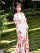 A woman in a white kimono standing in a garden.