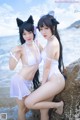 Two women in white bikinis posing on a rock by the ocean.