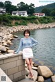 A woman in a blue sweater and white skirt posing by the water.