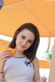 A woman in a white tank top holding a piece of orange.