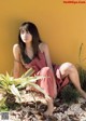 A woman in a pink dress sitting on the ground next to a plant.