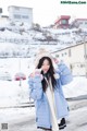 A woman in a blue coat and hat standing in the snow.