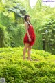 A woman in a red dress standing in the middle of a forest.