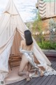 A woman sitting in front of a teepee on a wooden deck.