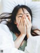 A woman covering her face with her hands in bed.