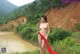 A naked woman standing next to a river with a red scarf.