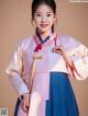 A woman in a pink and blue hanbok poses for a picture.