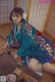 A woman in a blue kimono sitting on the floor.