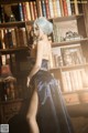 A woman in a black dress standing in front of a bookshelf.